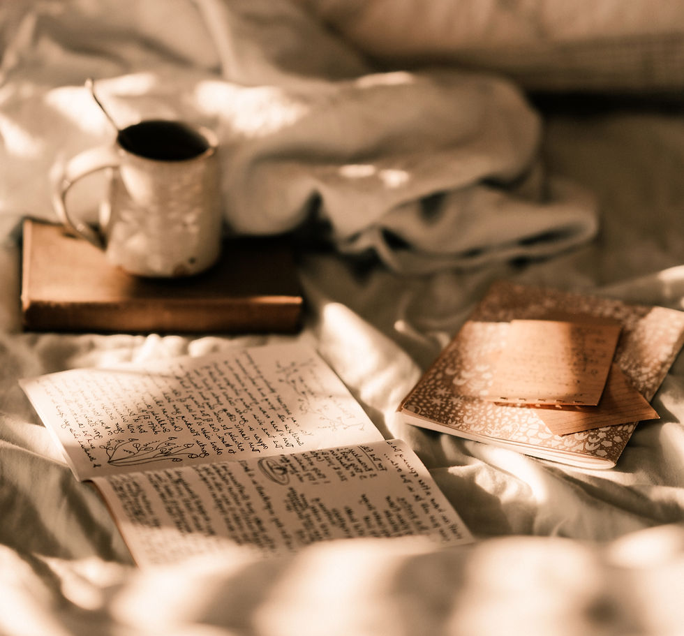 papers and books scattered over a bed with messy sheets and a cup with a hot beverage in the background