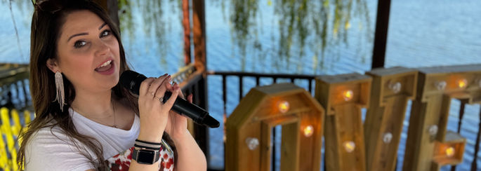 Hollie Marie singing by the water at Grendon Lakes wedding venue. with LOVE letters behind. wedding ceremony
