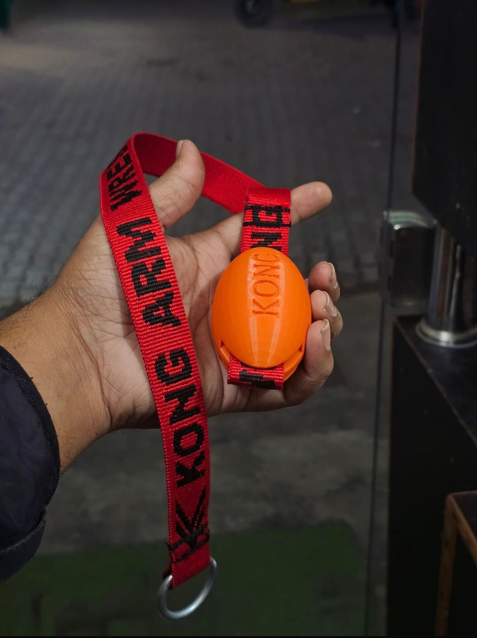 Hand holding orange Kong Arm Wrestling weight with Kong Strap 5.0