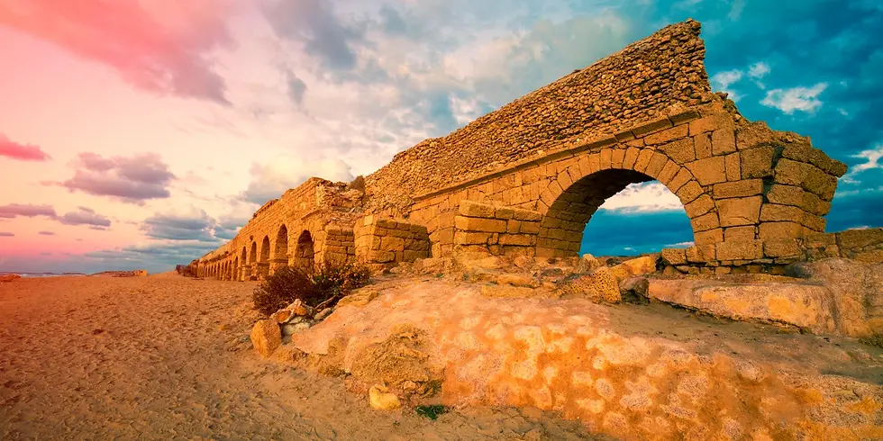The ancient aqueduct of Caesarea, Israel, made up of brown stones and archways against a pink and blue sky