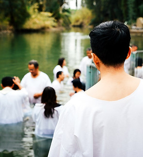 Christian pilgrims in white robes are baptized in the waters of the Jordan River