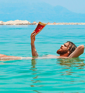 A man floats on his back in the Dead Sea, reading a book, alone.