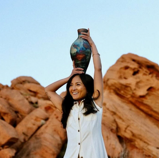 ceramacist holding her vase on top of her head with red rocks in the background