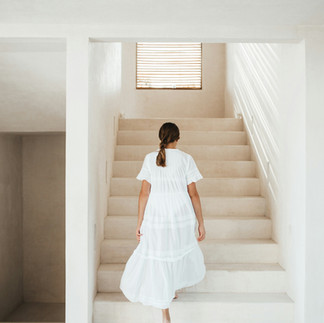 girl with braided ponytail walking up stairs wearing white dress