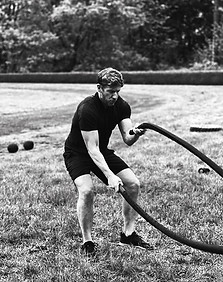 Precise Alt Text: A focused man of varied age using battle ropes in an outdoor park workout, building foundational strength at Dad Bod Strong Fitness.