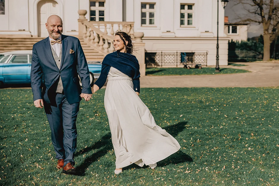 lenerowa ceremonia pod błękitnym niebem, wejście Pary Młodej wśród kwiatów, ikoniczny Cadillac Sedan DeVille przed pałacem, pałacowe wnętrza pełne blasku.