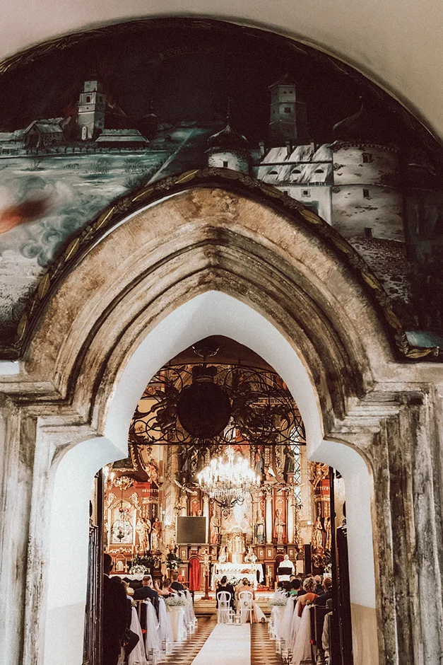 Para Młoda stojąca przed ołtarzem, otoczona rodziną i przyjaciółmi, w momencie składania przysięgi.