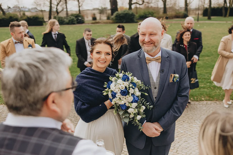 lenerowa ceremonia pod błękitnym niebem, wejście Pary Młodej wśród kwiatów, ikoniczny Cadillac Sedan DeVille przed pałacem, pałacowe wnętrza pełne blasku.