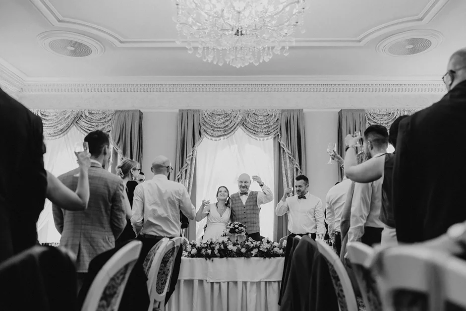 lenerowa ceremonia pod błękitnym niebem, wejście Pary Młodej wśród kwiatów, ikoniczny Cadillac Sedan DeVille przed pałacem, pałacowe wnętrza pełne blasku.