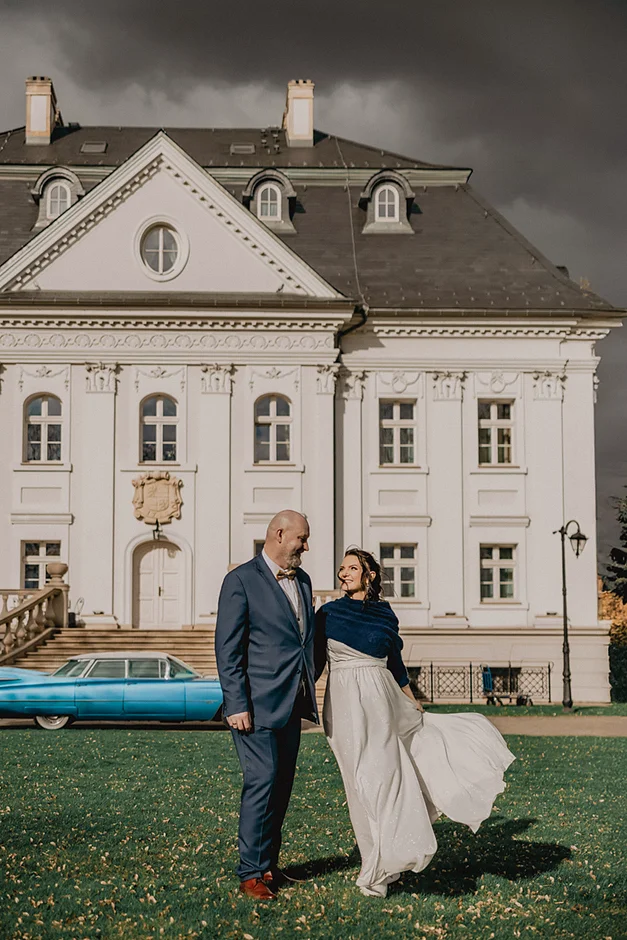 lenerowa ceremonia pod błękitnym niebem, wejście Pary Młodej wśród kwiatów, ikoniczny Cadillac Sedan DeVille przed pałacem, pałacowe wnętrza pełne blasku.