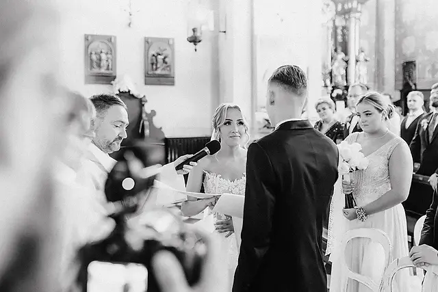 Para Młoda stojąca przed ołtarzem, otoczona rodziną i przyjaciółmi, w momencie składania przysięgi.