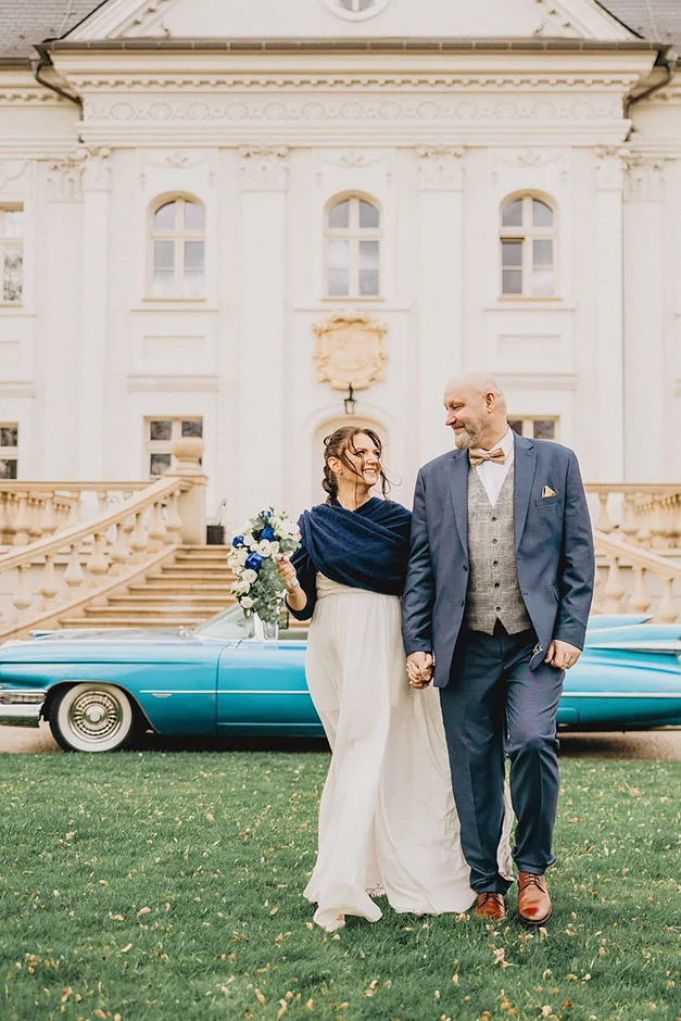 lenerowa ceremonia pod błękitnym niebem, wejście Pary Młodej wśród kwiatów, ikoniczny Cadillac Sedan DeVille przed pałacem, pałacowe wnętrza pełne blasku.