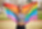 Person wearing marathon medal and holding pride flag outstretched behind them, smiling.