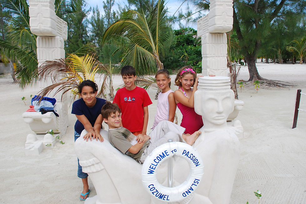 A group of children relished a sunny day at Passion Island, Cozumel, Mexico, as they gathered around Chac Mool amidst the sandy tropical setting.