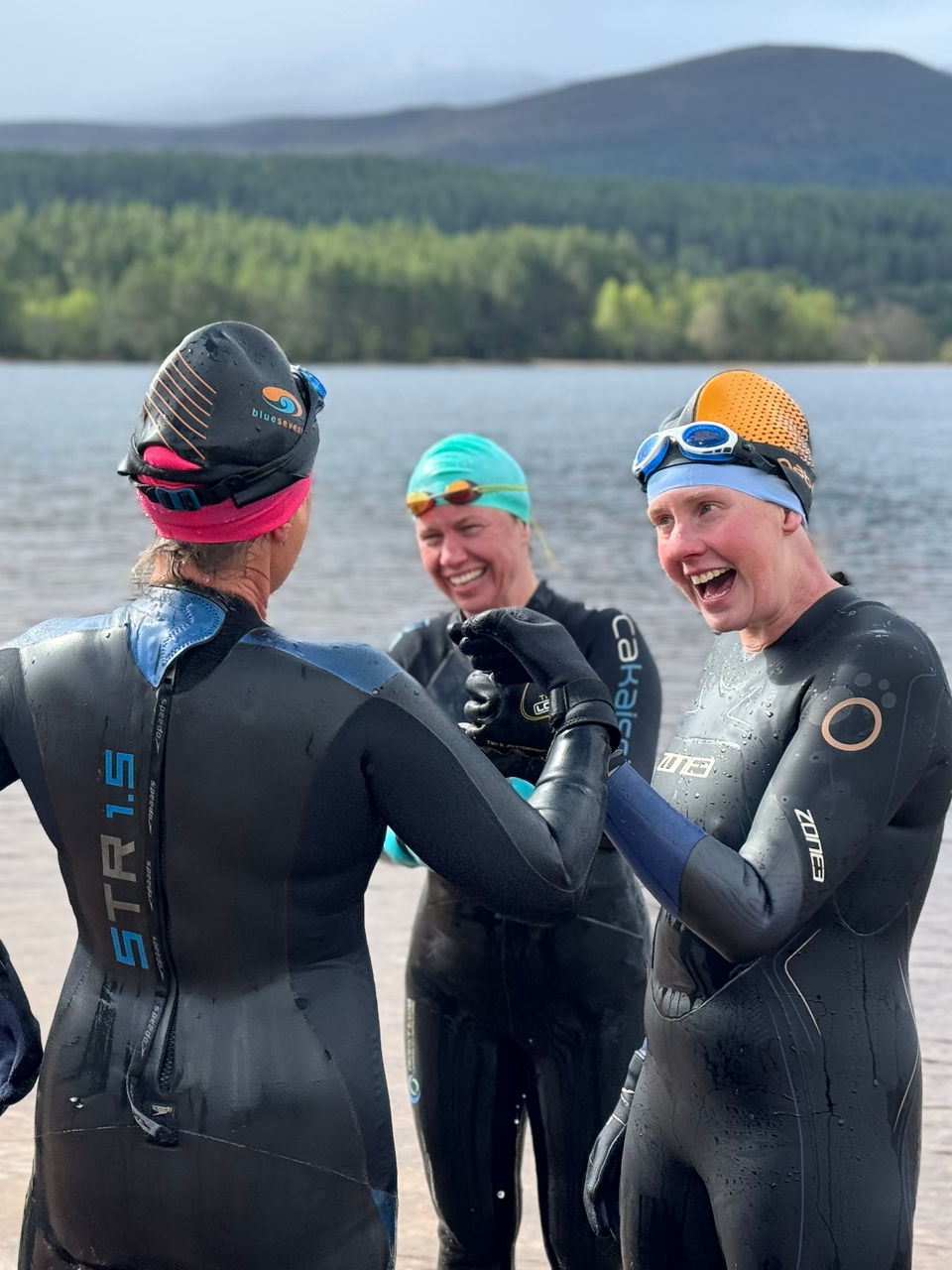 Open water swimmers in wetsuits talking during a coaching briefing by a loch