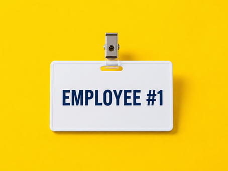 Employee name badge reading “Employee #1” on a bright yellow background, representing hiring your first employee.