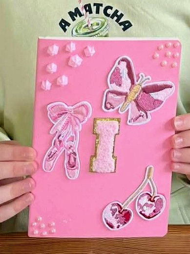 Close up of a pink notebook, with initial patch and decorative patches and charms.