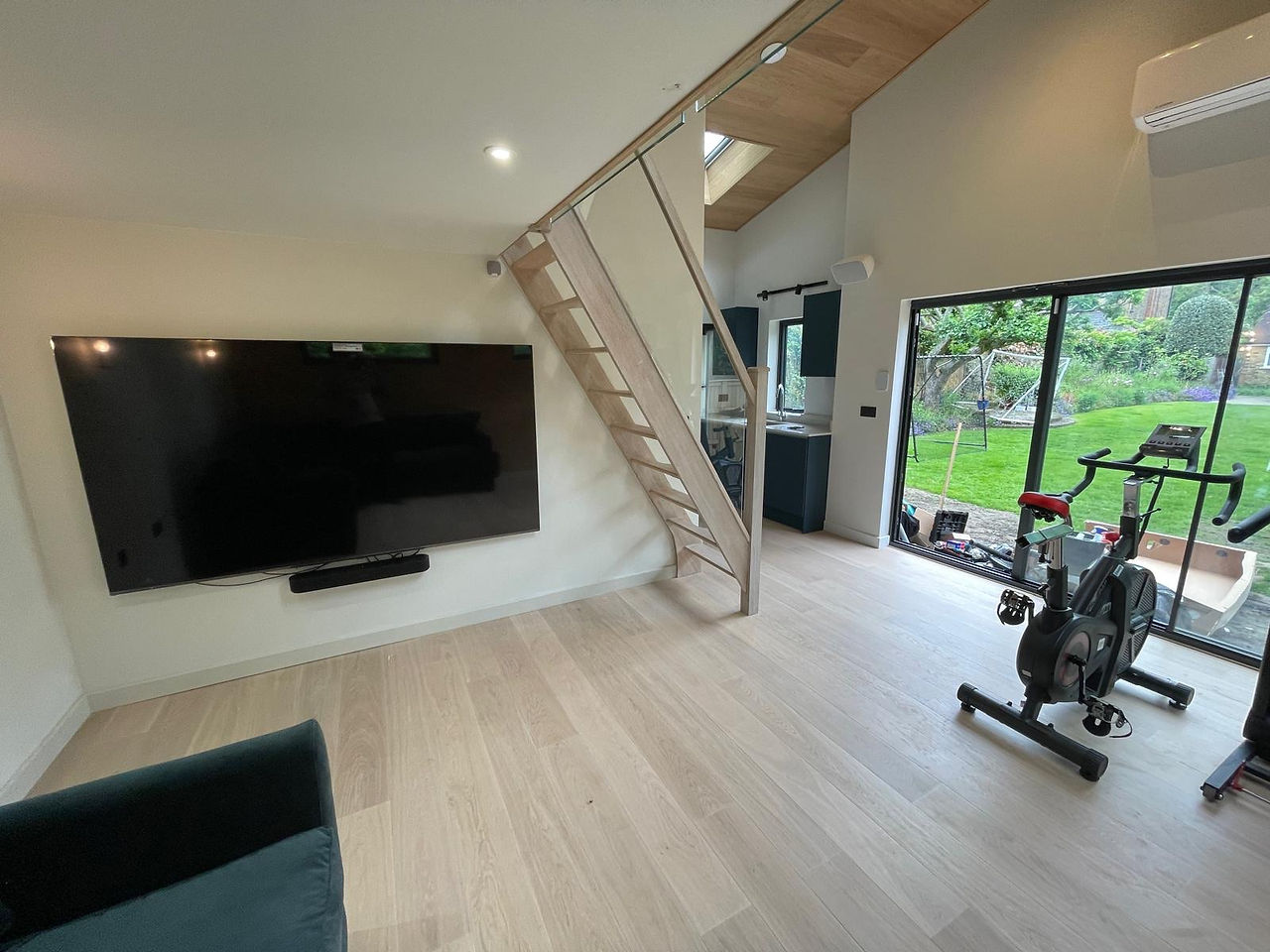 Lounge area with corner sofa and TV beneath mezzanine floor in modern garden studio Surbiton.