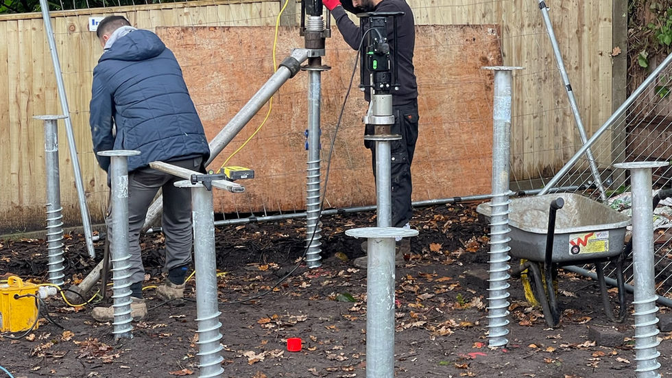Builders installing galvanised screw pile foundations for a bespoke cedar-clad garden stud