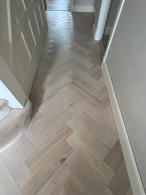 Close-up of light oak herringbone flooring meeting carpeted staircase in London property, showing neat edging and clean lines