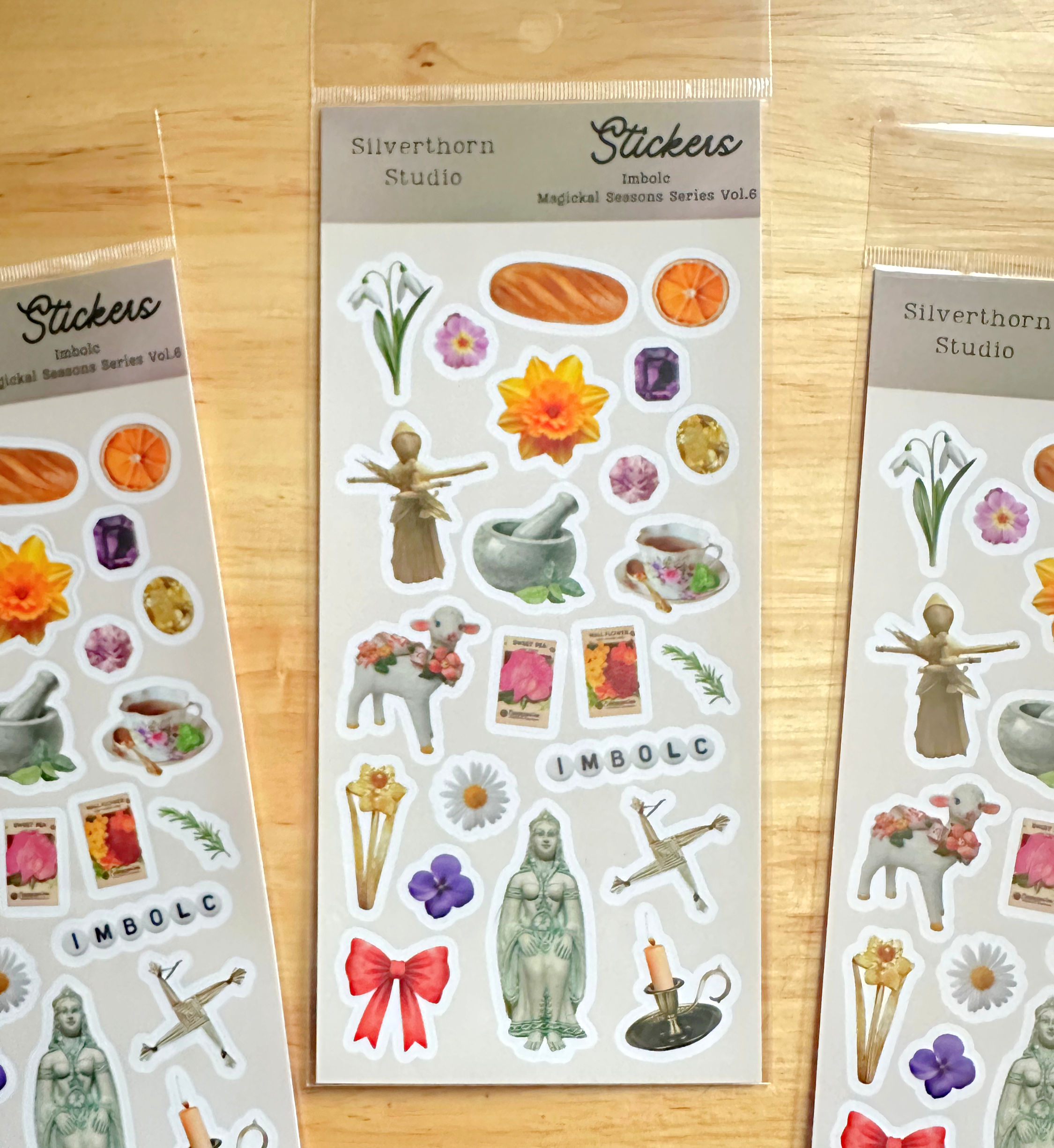 Sticker sheets featuring mystical and nature-themed elements, including flowers, crystals, candles, and a scarecrow, are arra