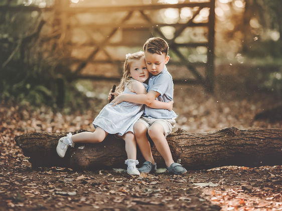 sister-cuddling-her-brother-on-a-trunk-in-woods.jpg