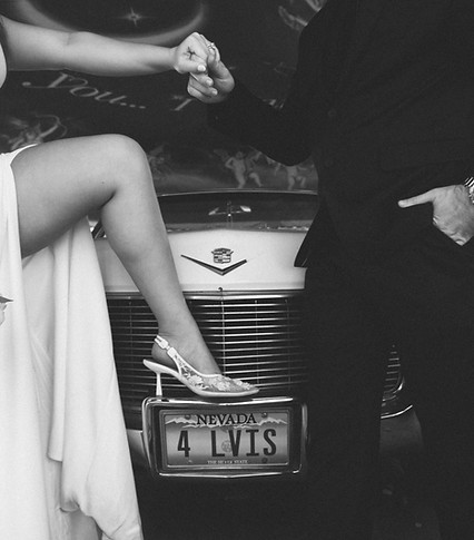 Bride standing with heel on pink Cadillac holding groom’s hand outside The Little White Chapel in Las Vegas.