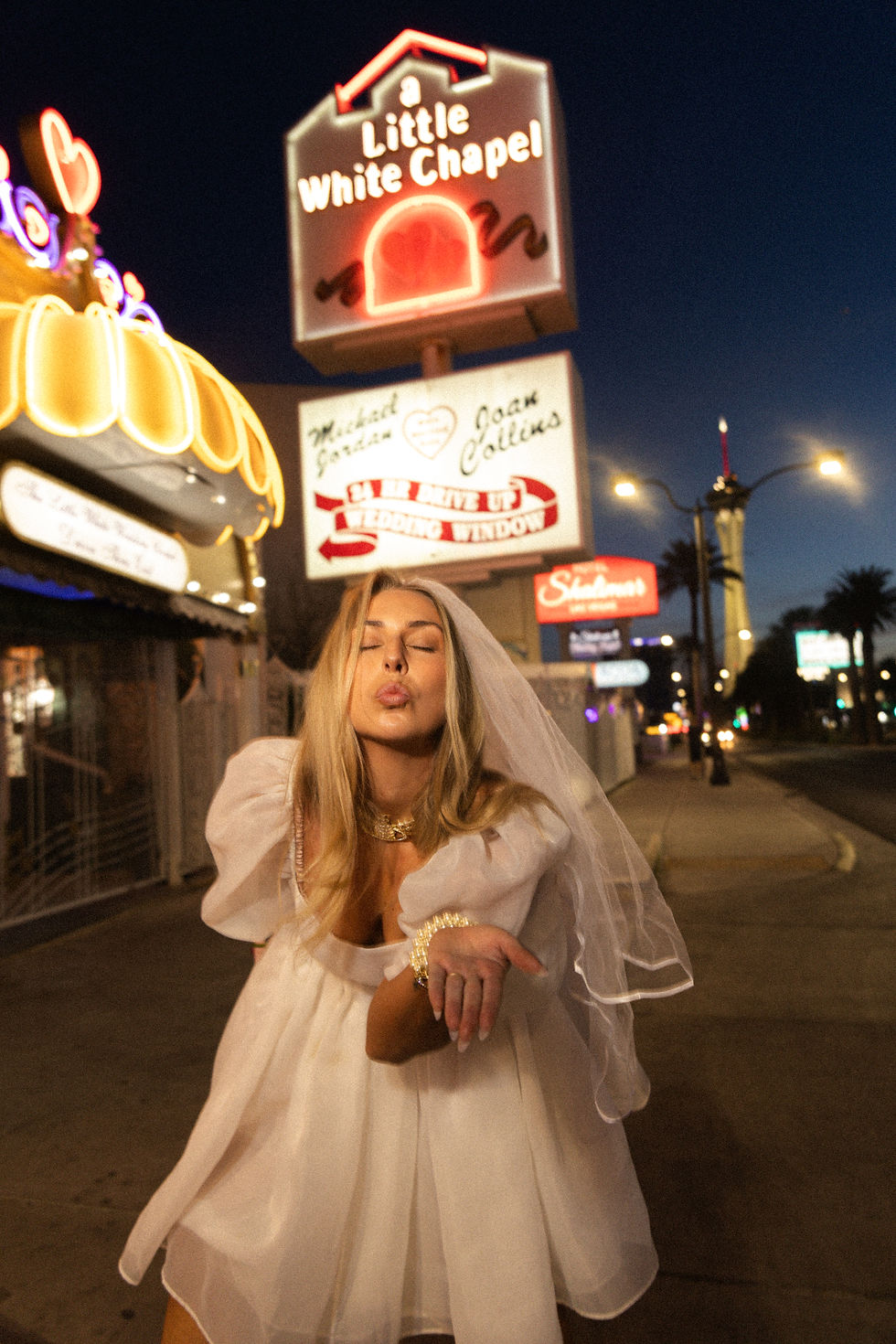 Bride blows a kiss at the camera in front of the iconic Little White Chapel neon sign at night on Las Vegas Blvd.