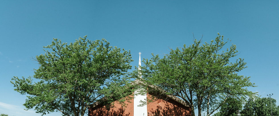 exterior view of the apse of the church with the steeple centered between two trees