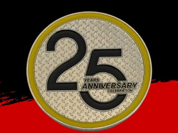 Silver, round challenge coin with a grilled texture, featuring "25th Anniversary" engraved on its surface.