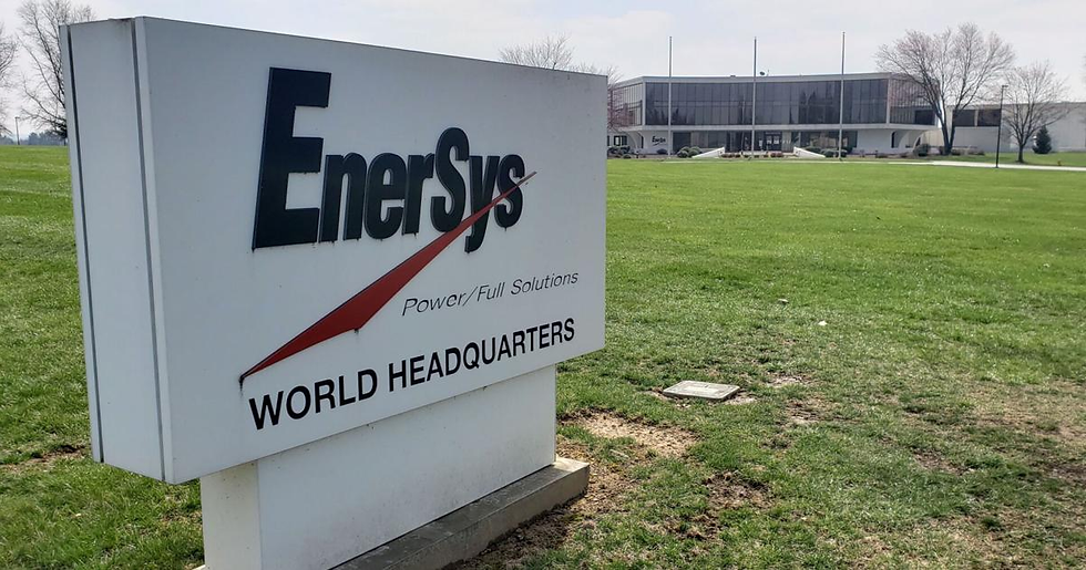 Sign reading "EnerSys World Headquarters" on a grassy lawn. A large office building is visible in the background under a clear sky.
