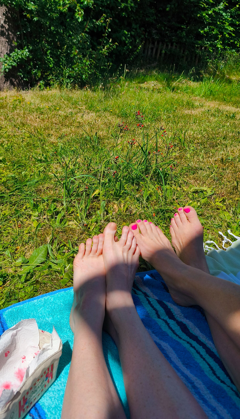 Zwei Freundinnen sitzen barfuß auf einer Decke im sonnigen Garten. Ihre Füße ruhen auf dem sattgrünen Gras – ein Moment der Verbundenheit, Leichtigkeit und Erdung.
