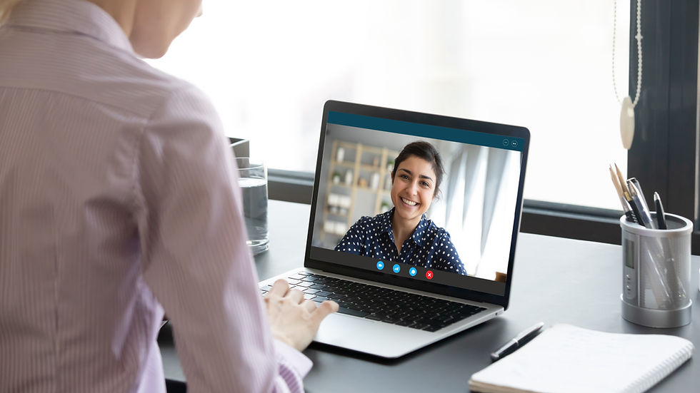 Person in striped shirt on a video call with a smiling woman on laptop screen. Desk with notebook, pen, and window in the background.
