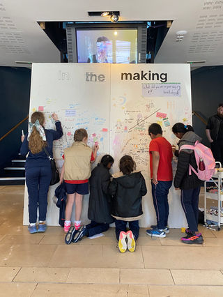 Six children drawing on a large white wall labeled "In the Making."