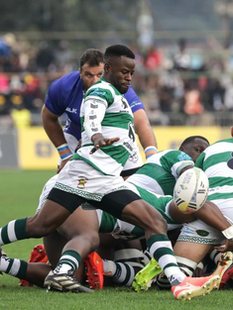 Zimbabwe rugby captain Hilton Mudariki lifts the Africa Cup trophy in celebration as the Sables qualify for the 2027 Rugby World Cup, ending a 34-year drought. Teammates cheer around him in their green-and-white kits at Mandela National Stadium in Kampala after a dramatic 30–28 win over Namibia.