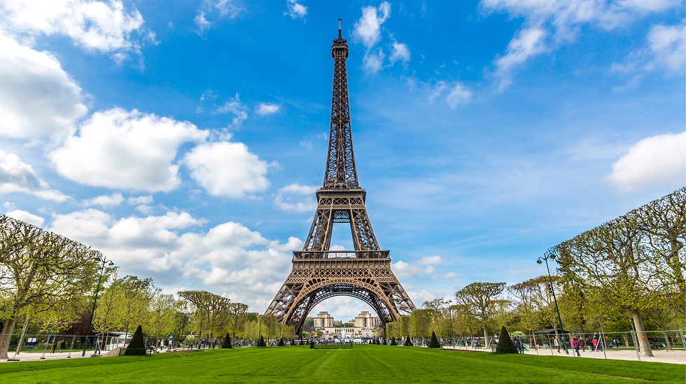 青い空の下にエッフェル塔。緑の芝生と木々が広がる公園。雲が点在し、明るく穏やかな雰囲気。