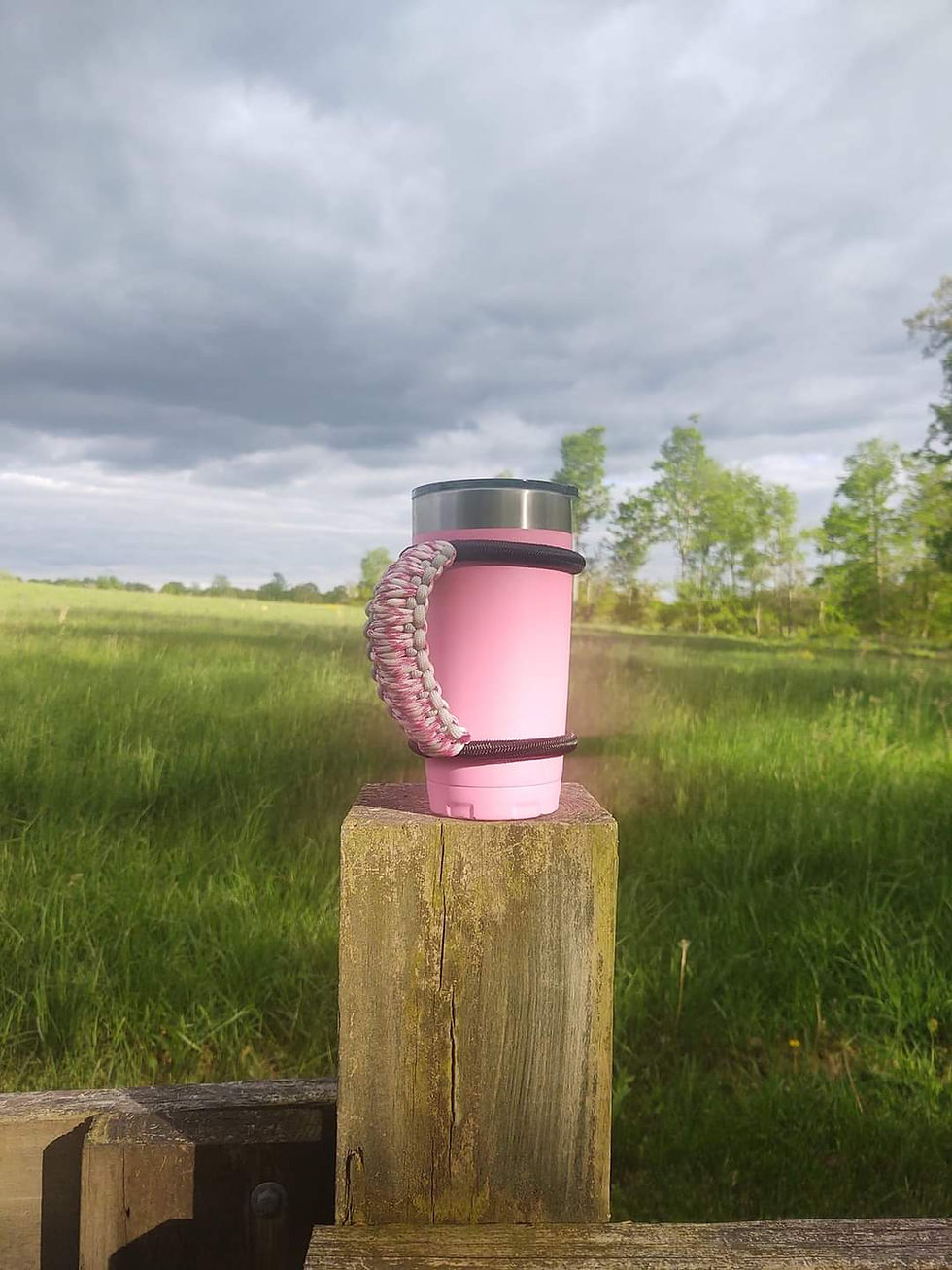 Pink mug with a paracord handle resting on a fence