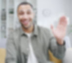 Smiling man waves hello in a casual shirt and background.