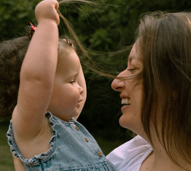 mom and daughter embracing while 1 year old plays with mommy's hair