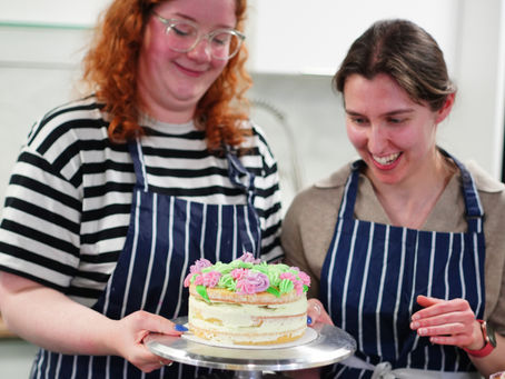 Two women holding up pink and green decorate cake they have made at Bake Master London class