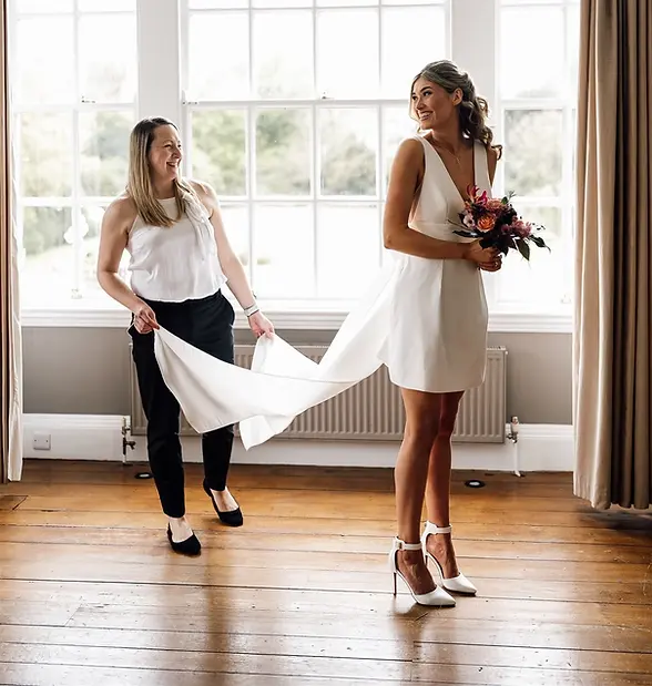 Wedding planner adjusting the dress of a bride with a colourful bouquet as she prepares to