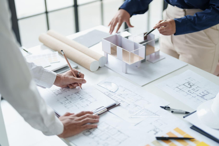 Architetti chini su planimetrie e un modello bianco mentre disegnano piante su un tavolo