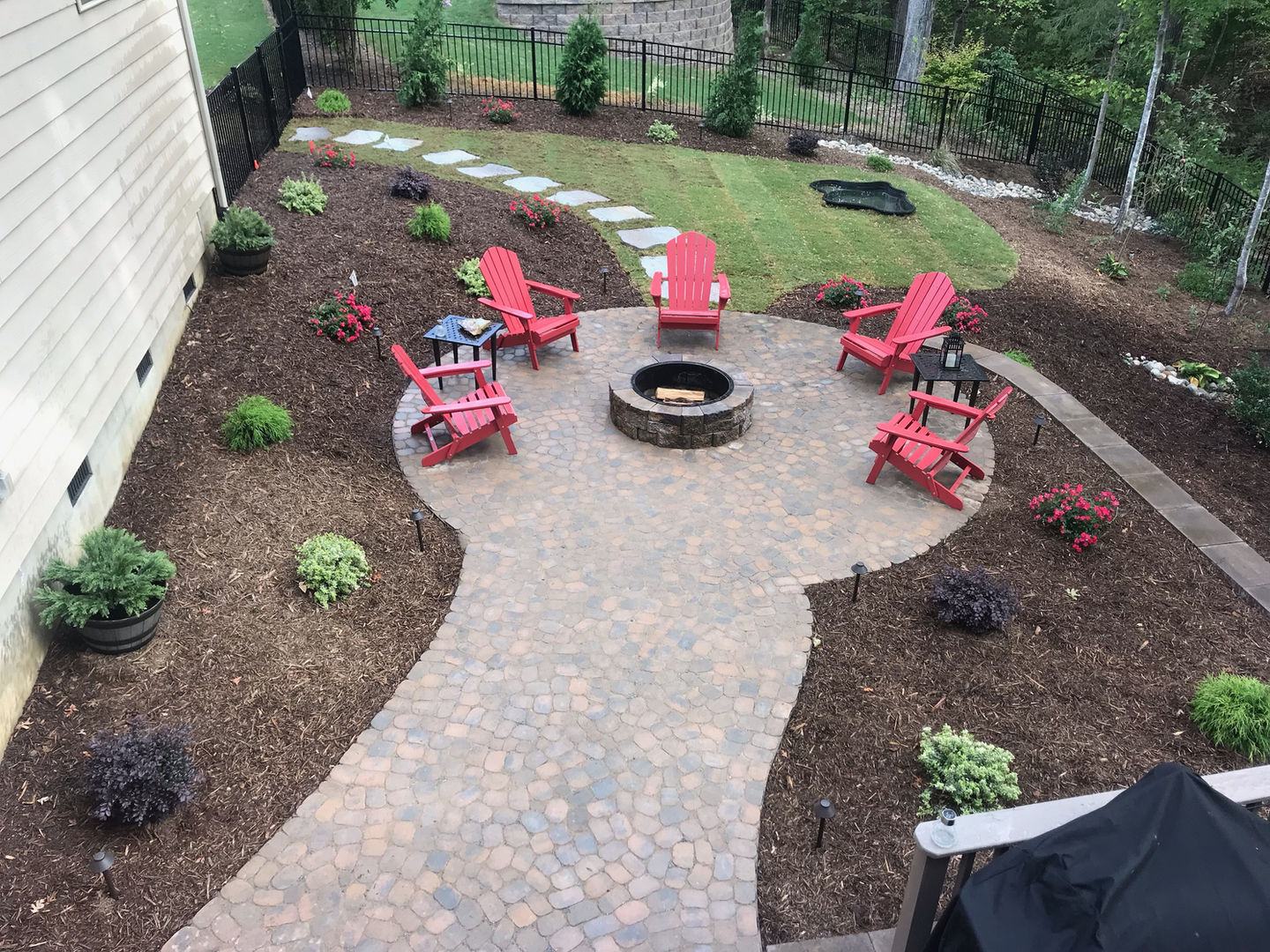 Large patio with stone pavers, fire pit, and red chairs.