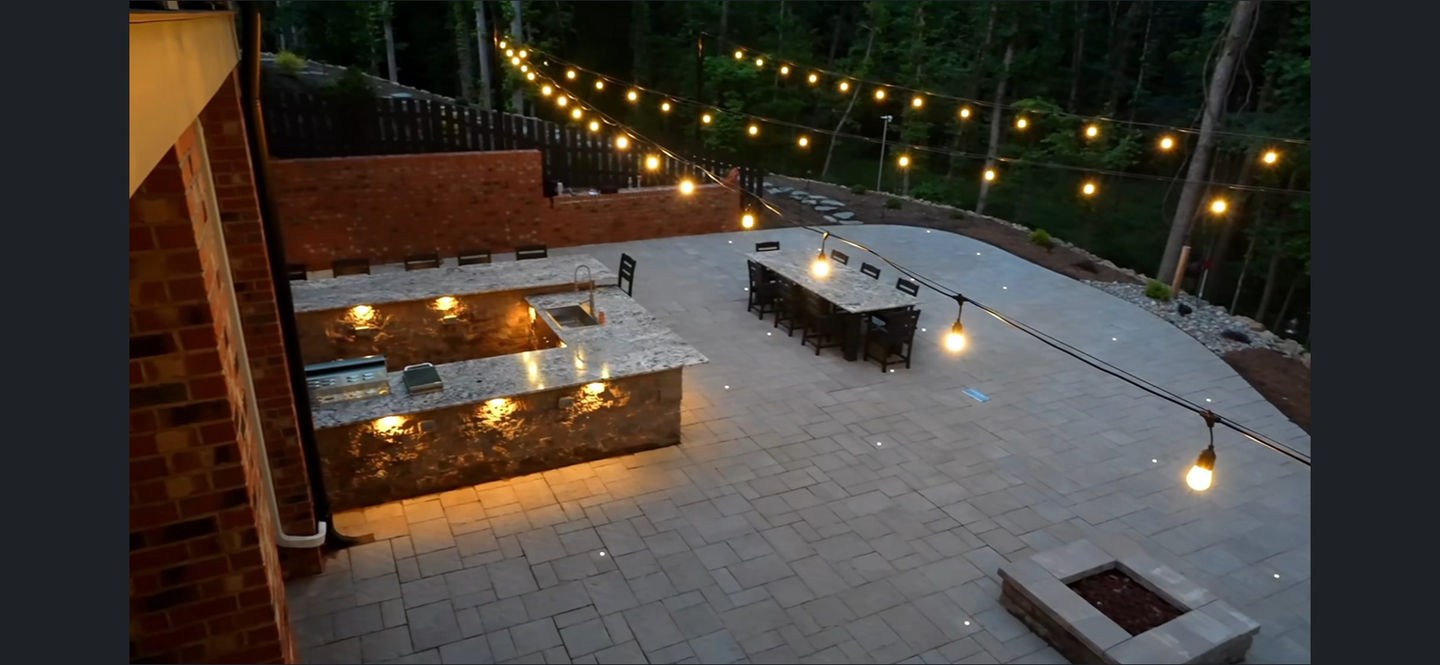 Large patio with outdoor kitchen and string lights at night