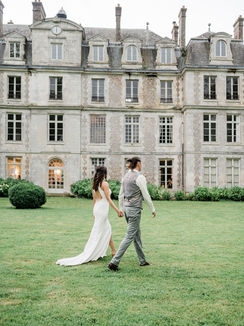 Couple de mariés marchant derriere la facade du château de Brumare, en extérieur