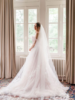 Mariée debout devant une grande fenêtre, lumière naturelle douce, photographie de mariage fine art