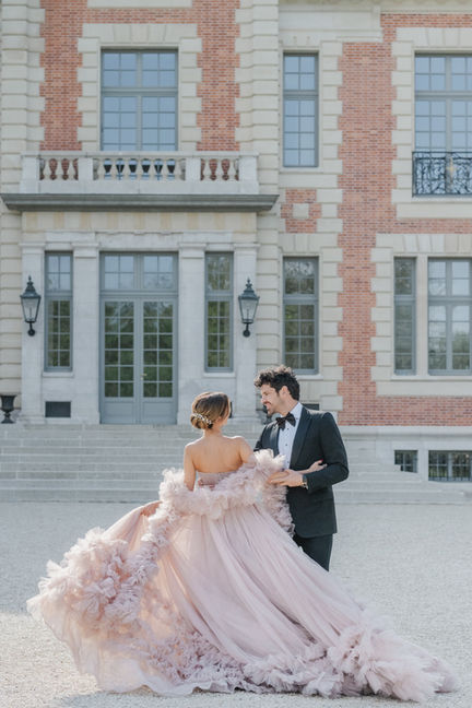 Couple posant devant un château, la mariée en robe volumineuse.