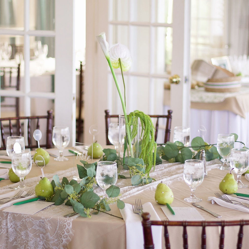 Elegant wedding table setting with green foliage, calla lilies, pears as place card holders, and a lace table runner.