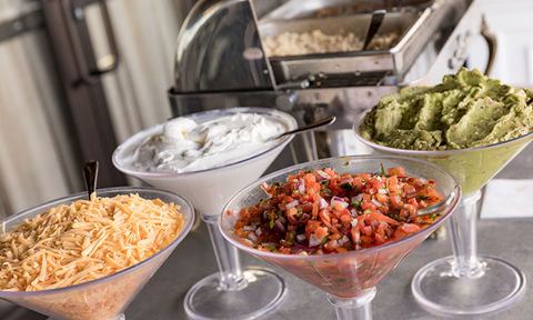 Taco bar toppings in martini glasses, including shredded cheese, sour cream, pico de gallo, and guacamole.