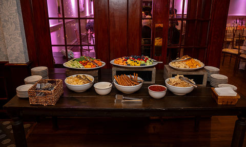 Appetizer station on a dark wood table displaying fresh fruit, vegetables, cheese, chips, and dips.